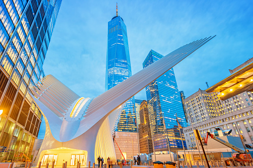 People walk beside the The Oculus, the new World Trade Center Transportation Hub building and One World Trade Center in Lower Manhattan, New York City USA at twilight.