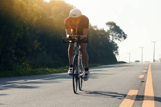 the triathlete comes along the sunny road in a scene with flare - road cycling imagens e fotografias de stock