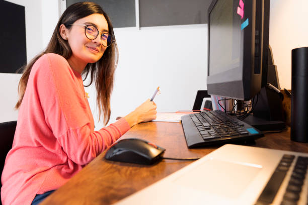 istock Latin woman sitting at her desk taking notes while looking at the camera 1250547422