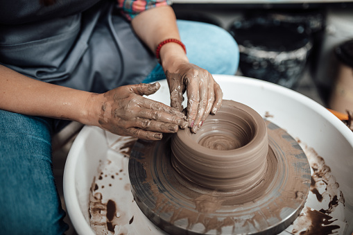 Female artist sculptor or potter making clay pottery on a spin wheel.