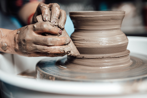 Female artist sculptor or potter making clay pottery on a spin wheel.