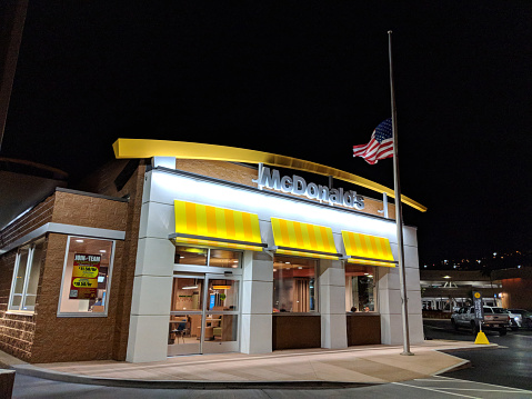 Honolulu - April 14, 2018: McDonalds Store at night with flag at half mast above welcome sign and logo in Honolulu, Hawaii.  McDonald's primarily sells hamburgers, cheeseburgers, chicken, french fries, breakfast items, soft drinks, milkshakes, desserts.