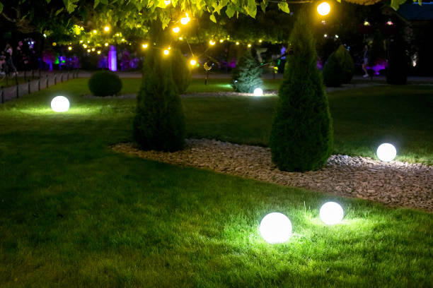 istock illumination backyard light garden with electric ground sphere lantern with stone mulch and thuja bush in outdoor landscaping park with garland warm light bulbs, dark illuminate night scene closeup. 1250557246