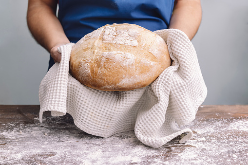 hands of an unrecognizable person holding a loaf of freshly baked bread, concept of healthy eating at home