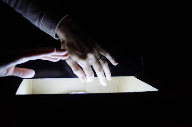 istock Woman's hands opening a light box on dark background. Mistery, surprise or suspense concept. 1250561382