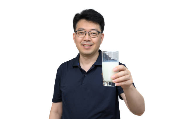 A middle-aged Asian man is drinking a fresh glass of milk on white background. stock photo