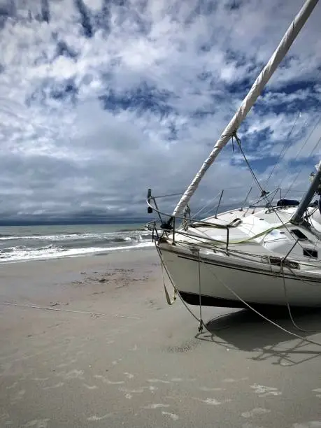 A sailboat marooned on the beach until the next tide comes in on a bright sunny summer day with clouds.