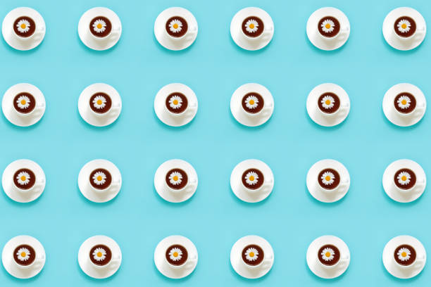 Pattern made from white cup of tea with chamomile on dish saucer, blue background. Top view Flat lay.