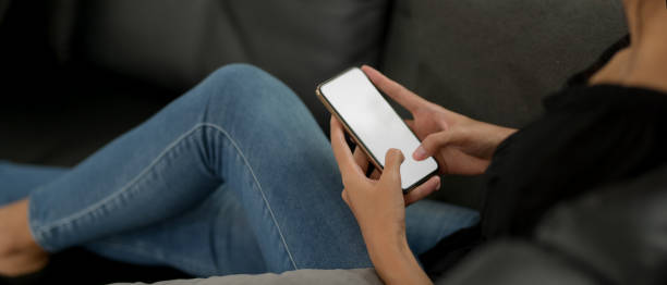 istock Female using mock-up smartphone while lying on the black couch in living room 1250571361