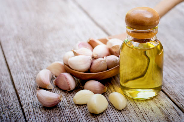 Garlic oil Garlic cloves with extract essential garlic oil in glass bottle isolated on rustic wood table background. cooking with garlic stock pictures, royalty-free photos & images