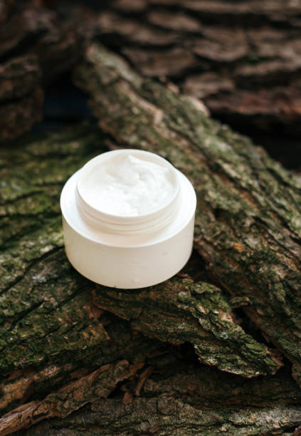 istock Cosmetic cream jar on tree bark piece side view. Organic cosmetology botanical concept. White plastic container with natural moisturizing balm and greenery. Female skin care accessory 1250582957