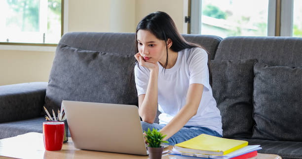 istock Asian woman, happy cheerful cute beautiful is using a notebook computer and sitting on a sofa for working from home. She is quarantined at home during the coronavirus epidemic. And she has sanitizer gel on the table for cleaning hands 1250589898