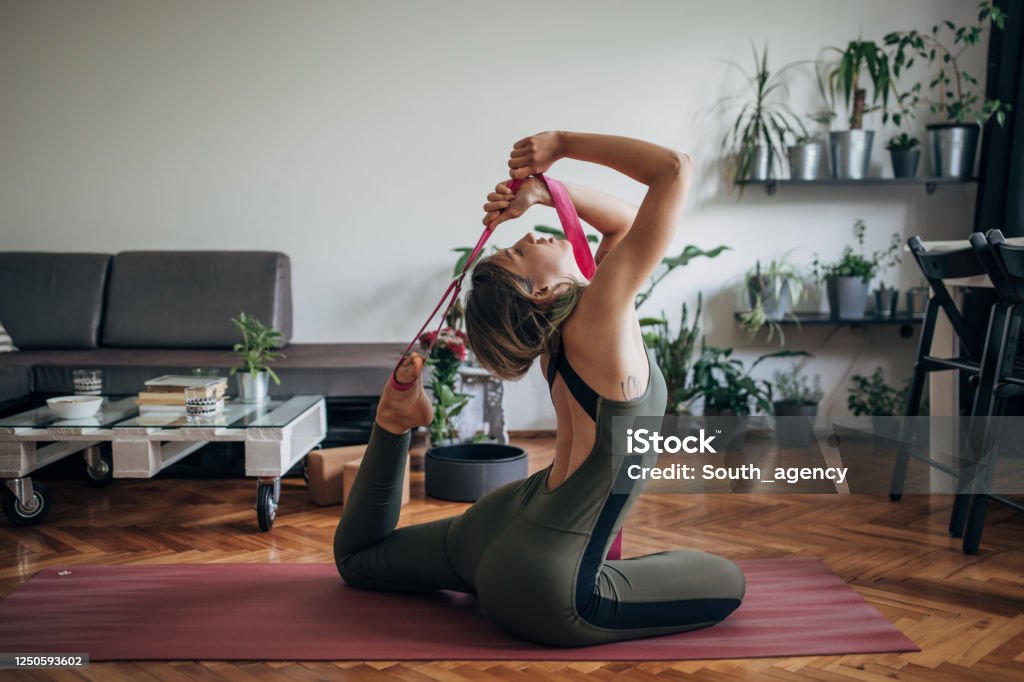 Young woman doing yoga on the floor in living room One woman, young woman doing yoga on the floor in living room at home alone. Flexibility Stock Photo