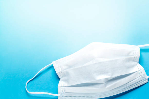 istock simple white air protection mask on the color surface on blue background. Disposable surgical face mask cover the mouth and nose. 1250593792
