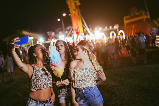 Pretty girls taking selfies with cotton candy in amusement park at night.