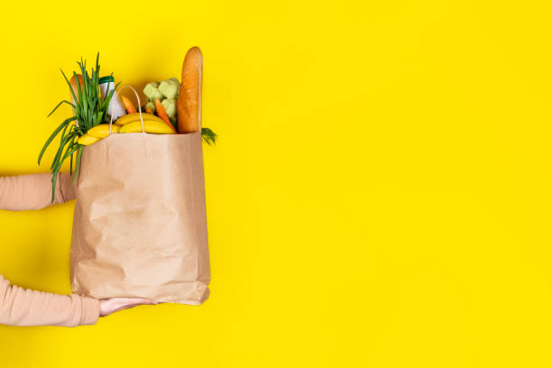 chica o mujer sostiene una bolsa de papel llena de alimentos como frutas, verduras, leche, yogur, huevos aislados en amarillo. - raw potato red potato red vegetable fotografías e imágenes de stock