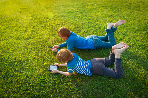 father and son with book and mobile phone on grass, summer relax in nature