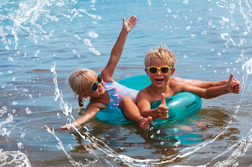 happy boy and girl splash water on beach, kids summer fun, family vacation