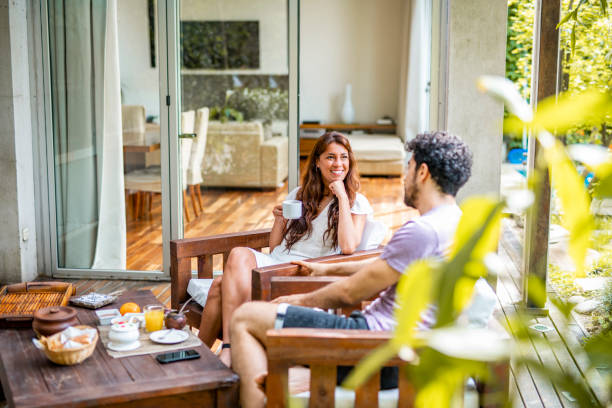 Mixed race and Hispanic couple in mid 20s and early 30s sitting side by side on outdoor deck enjoying breakfast and conversation.