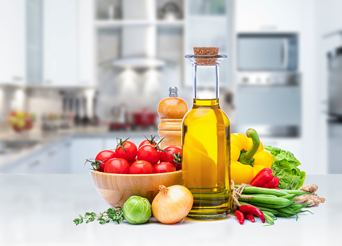 Healthy food: vegan ingredients on kitchen counter with defocused modern kitchen at background. The composition includes Cherry tomatoes, yellow bell pepper, onion, green beans, lettuce, ginger, chili pepper, extra virgin olive oil and a pepper mill. High resolution studio digital capture taken with Sony A7rII and Sony FE 90mm f2.8 macro G OSS lens