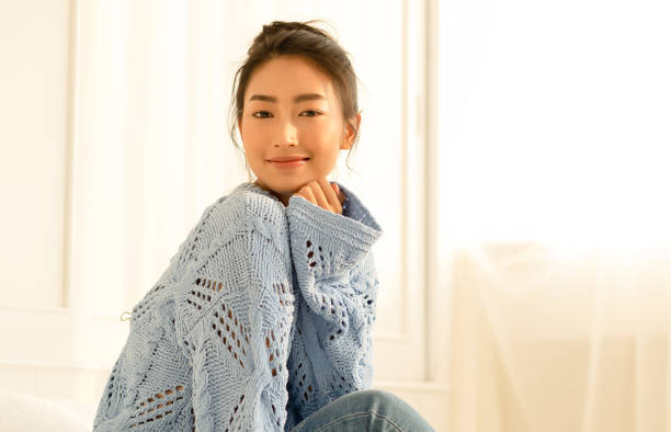 Portrait of beautiful young Asian woman smilling friendly and looking at camera in living room at home on a bright winter morning. Concept woman lifestyle and winter. Autumn, winter season. Portrait of beautiful young Asian woman smilling friendly and looking at camera in living room at home on a bright winter morning. Concept woman lifestyle and winter. Autumn, winter season. korea autumn stock pictures, royalty-free photos & images