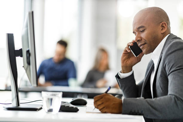 istock Smiling black businessman taking notes while talking on cell phone in the office. 1250617009