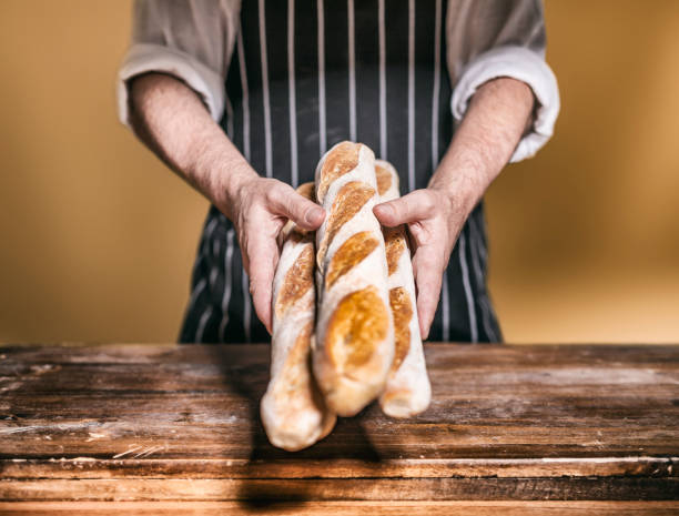 Baker offering baguette at bakery on wooden table