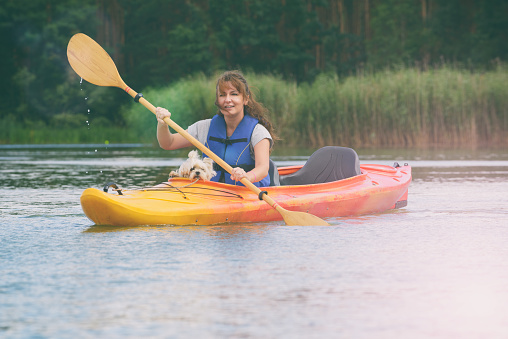 Beautiful woman is kayaking with her dog across the lake