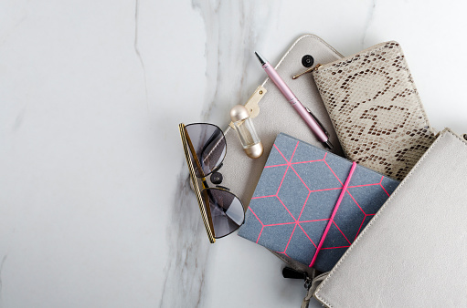 Closeup of woman bag, purse, sunglasses, notebook, pen, bottle of fragrance on the white marble table.Empty space