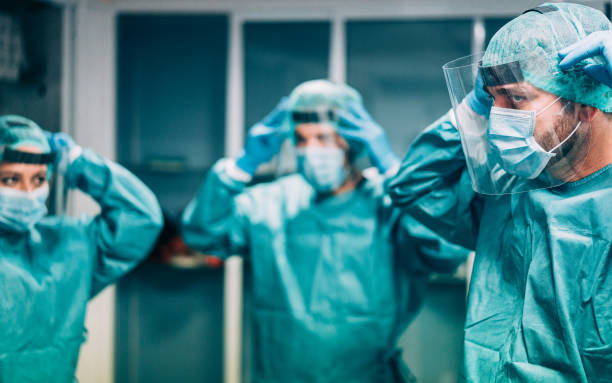코로나바이러스 전염병 발생 시 수술 수술을 위해 병원에서 일할 준비를 하는 의사와 간호사 - 진료소 내부에서 옷을 입고 있는 의료진 - 오른쪽 사람의 눈에 집중 - men women laboratory indoors 뉴스 사진 이미지