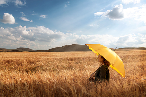 Rear view of woman with colorful umbrella standing in a wheat field.
