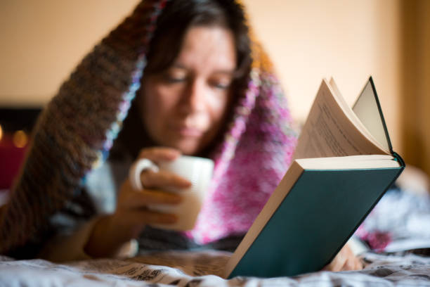 Reversed shot of young woman lying with a notebook on her belly and idyllic 1970s lighting overlays, she has long brown hair and looks into the camera