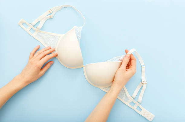 white bra in female hands. woman choosing holding white bra lingerie on blue background. flat lay with lace underwear bra. beautiful sexy full coverage bra. sale, special offer, lingerie store concept - panties lingerie sensuality bra imagens e fotografias de stock