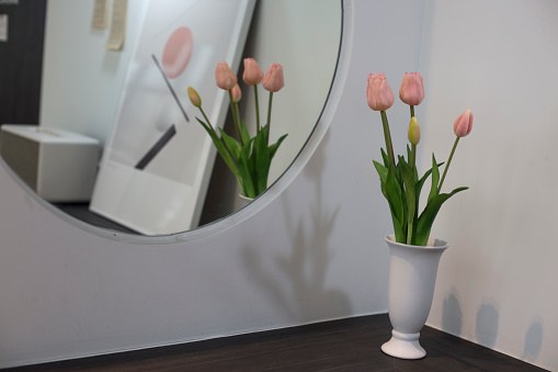 Beautiful pink tulips near mirror on wooden table