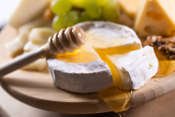Cheese plate, honey pouring on camembert cheese. On wooden background