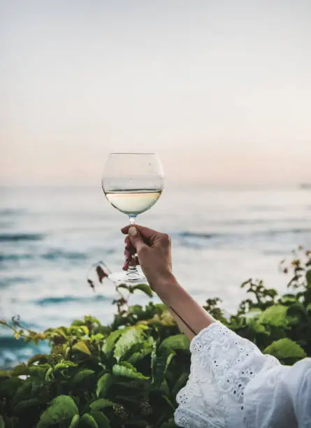 Photo of Woman holding glass of wine with sea and sunset background