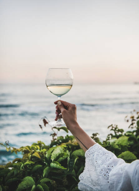 woman holding glass of wine with sea and sunset background - white wine wine white glass imagens e fotografias de stock