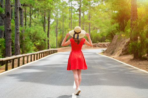 Woman in red dress and hat stand on the road in forest on a sunny day
