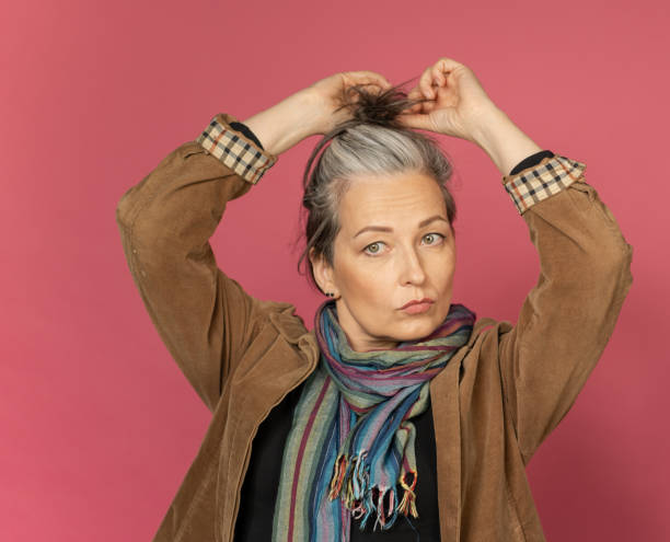 Mature gray-haired woman doing hairstyle. Creative Caucasian woman wearing casual clothes posing in studio on pink background Mature gray-haired woman doing hairstyle. Creative Caucasian woman wearing casual clothes posing in studio on pink background. pics for classic pin up poses stock pictures, royalty-free photos & images