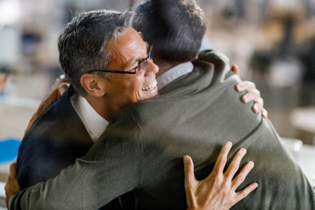 Happy male entrepreneurs embracing each other in the office. The view is through glass.