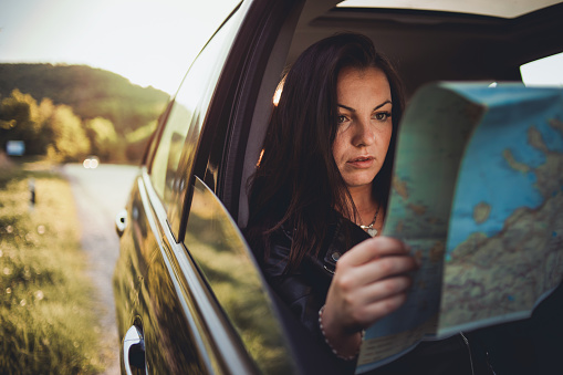 A young woman travels by car, looks at a map and enjoys the sunset