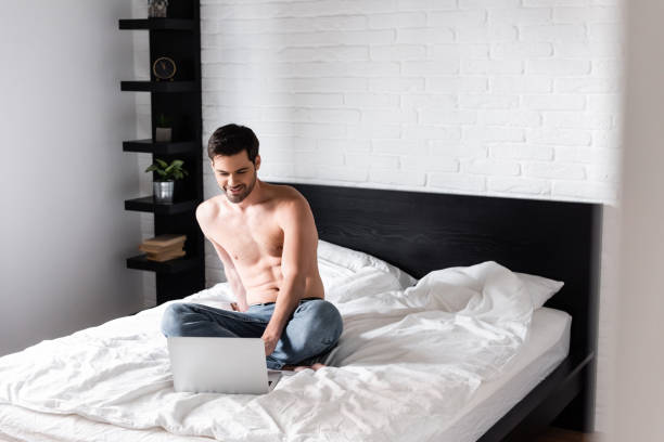 istock happy shirtless man networking on laptop in bed 1250655427