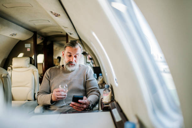 istock Company CEO using a smart phone and drinking wine while traveling aboard a private jet 1250661438
