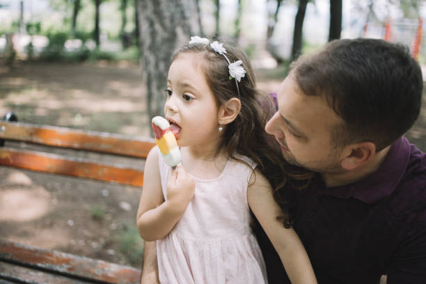 istock Daughter eating icecream while sitting on bench with her father 1250665982