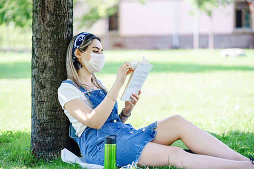 woman sitting in park (garden) on the green grass with smartphone, headphones, tablet and book in the hand