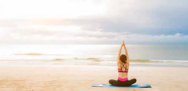 Photo of Young woman practicing yoga outdoor on the beach in morning