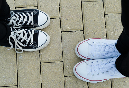 Teenagers with white and black sneakers standing on the paving, top view