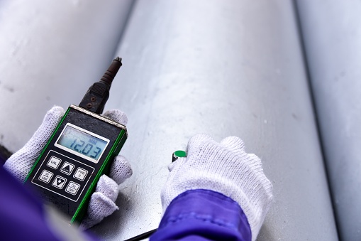 Inspector measuring thickness the pipe with UTM (Ultrasonic thickness measurement).  Selective focus on the inspection areas.