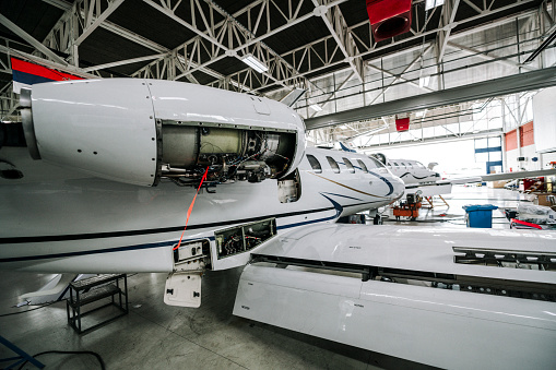 A small private jet with it's engine cover removed in a maintenance hangar.