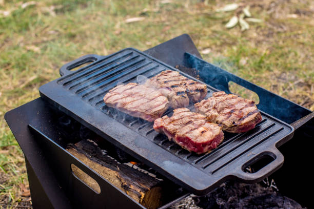 Beef steaks grilling on a cast iron plate on a camp fire. Campfire cooking. Outdoor BBQ. Beef steaks grilling on a cast iron plate on a camp fire. Campfire cooking. Outdoor BBQ blade roast stock pictures, royalty-free photos & images